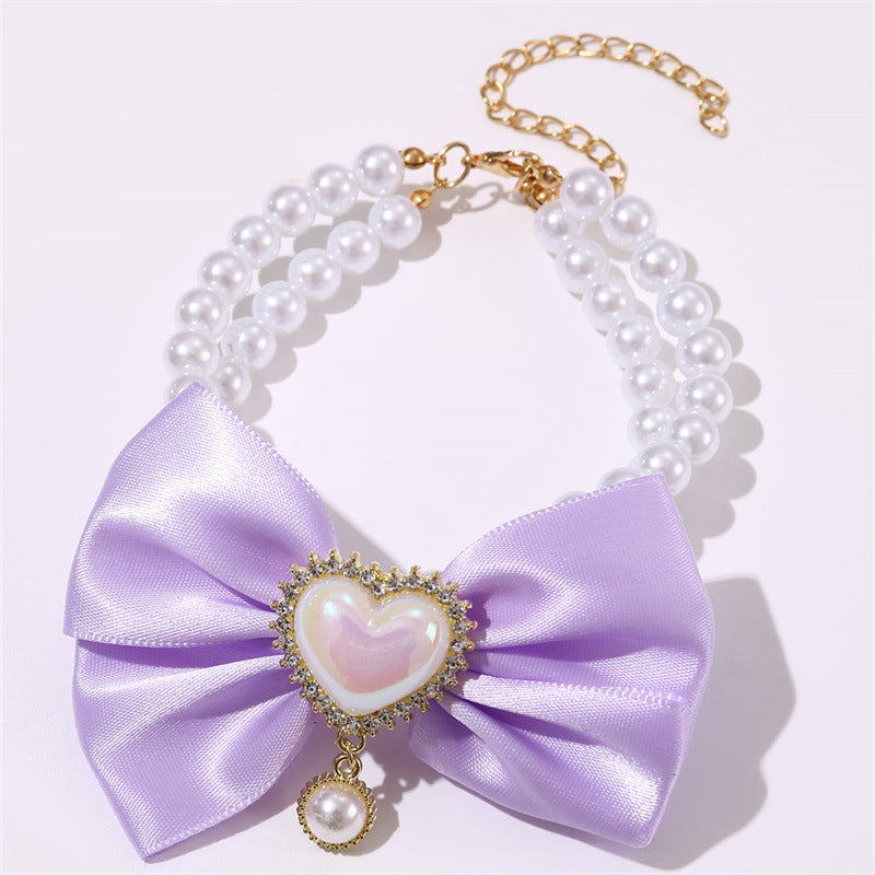 Necklace with a large purple bow and heart-shaped pearl pendant on a white background