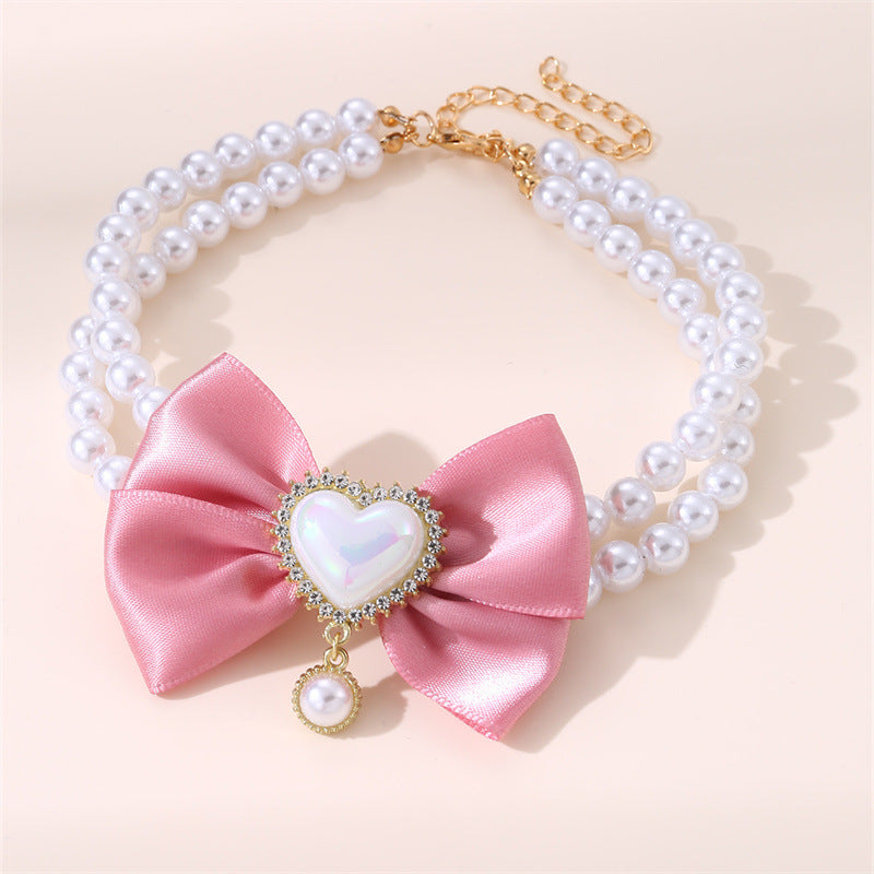 Necklace with pink bow and heart-shaped pearl pendant on a light pink background