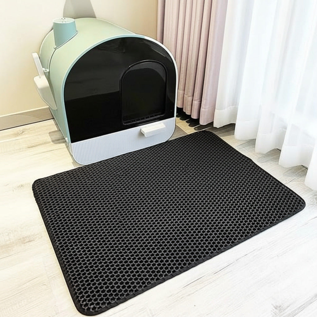 Black honeycomb mat in front of a cat litter box on a light wood floor.