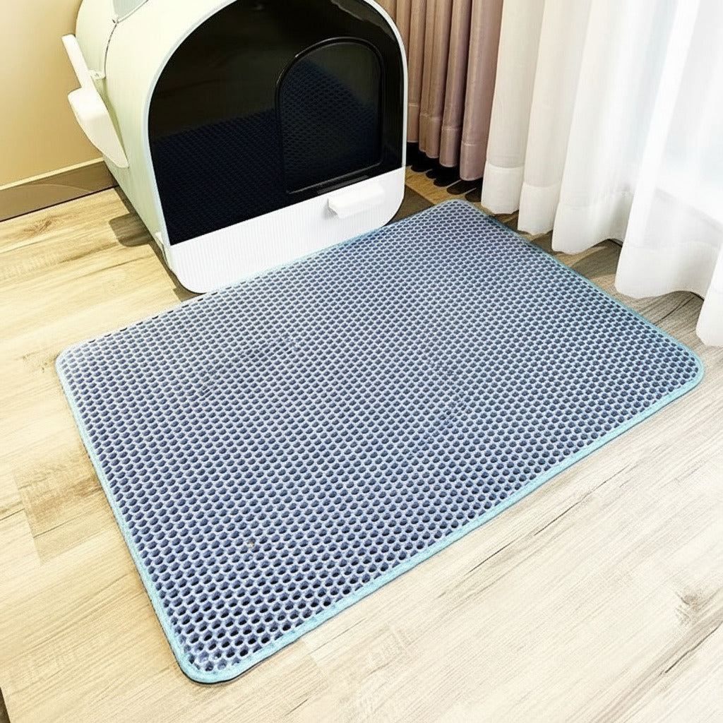 Blue mat with textured surface in front of a white litter box on a wooden floor.