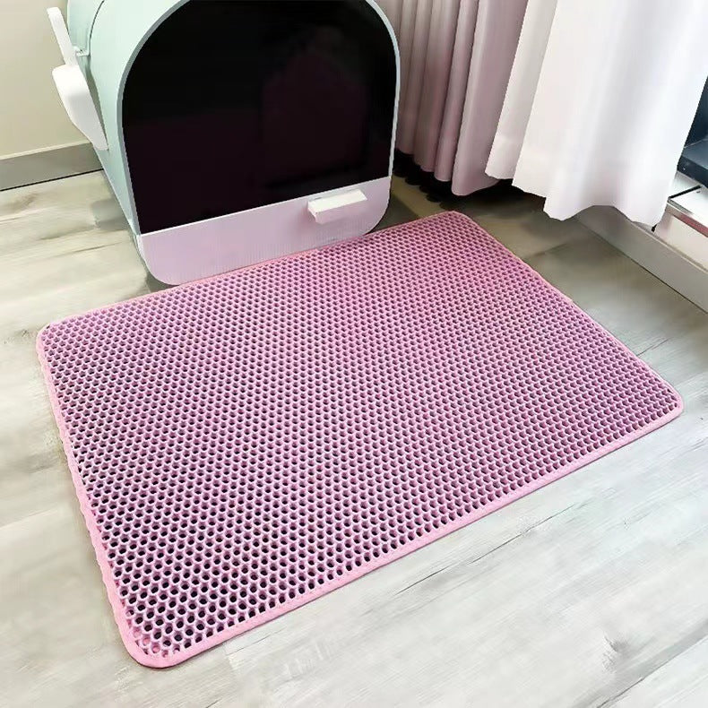 Pink mat with a textured pattern on a light wooden floor, next to a white pet litter box.